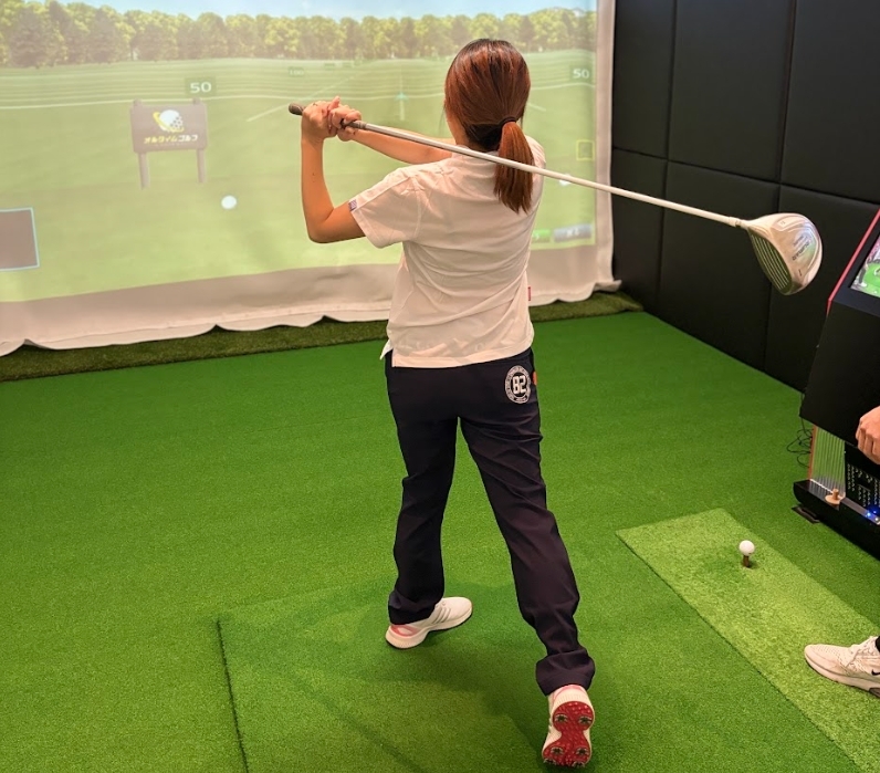 インドアゴルフ施設でドライバーの素振り練習を行う女性